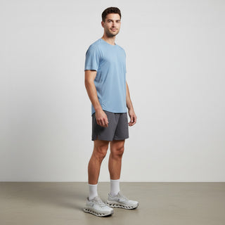 FWSports Shoes model wearing light blue t-shirt, grey shorts, and brown On Cloudtilt sneakers in a studio setting.